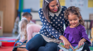 Teacher sitting on floor with young girl reading